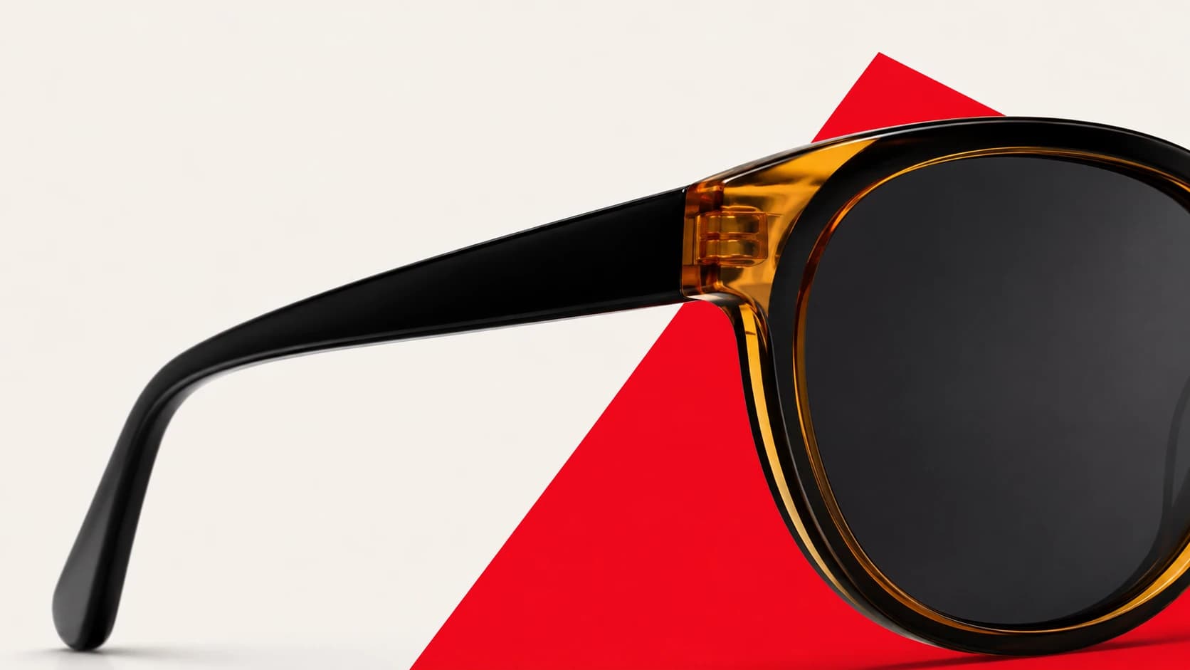 Close-up of glossy black sunglasses over a red geometric backdrop